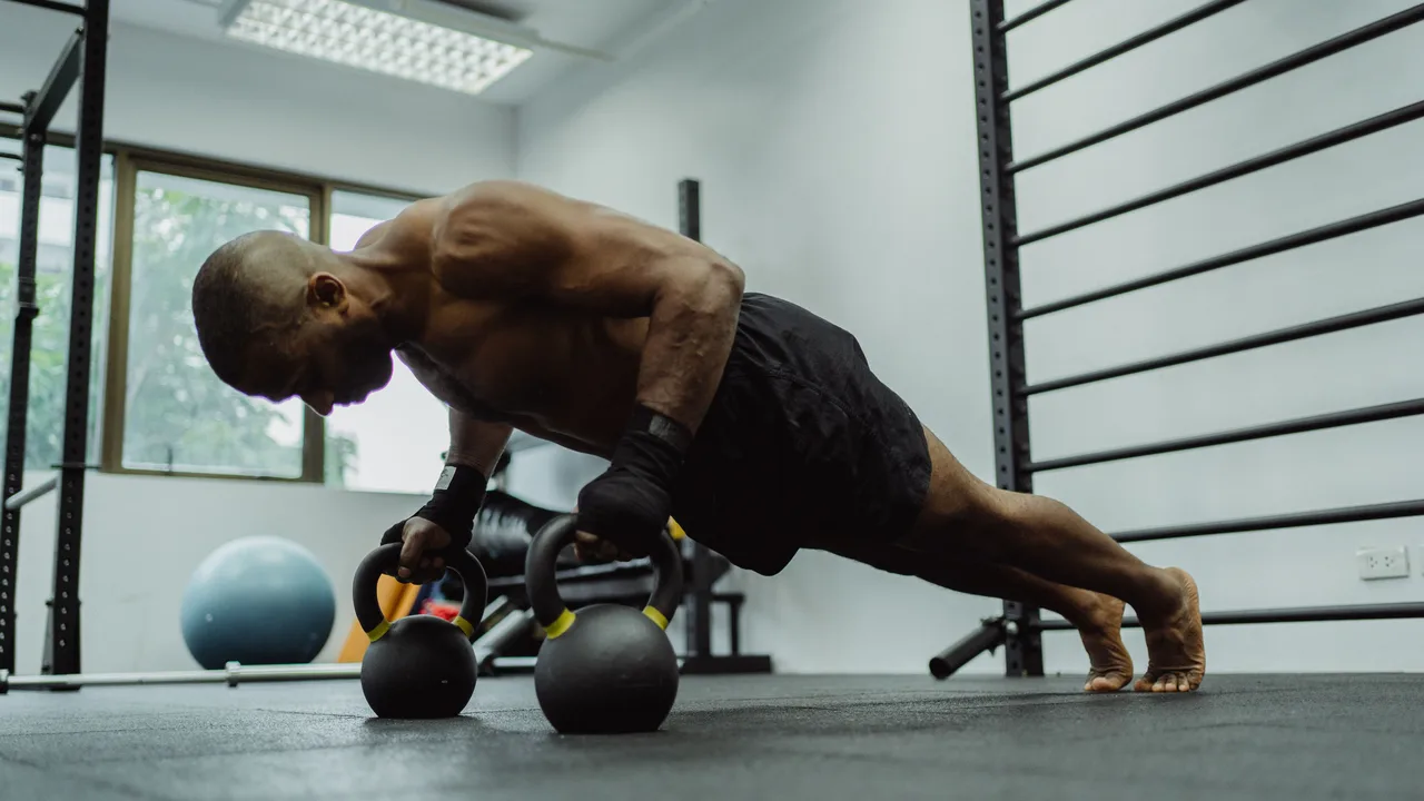 Homme réalisant des pompes avec des kettlebells illustrant l'entraînement en force pour la recomposition corporelle